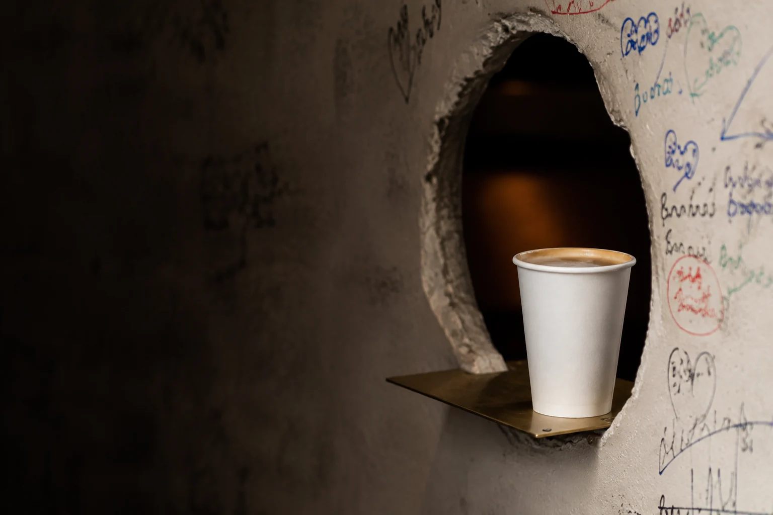 Imagen conceptual de un vaso blanco de café para llevar junto a un agujero y una pared con trazos de rotulador; no es una fotografía del local